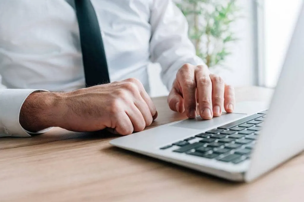 Businessman using laptop computer at office desk, hand on a trackpad or touchpad